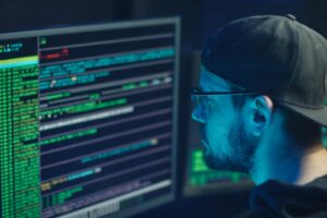 Un expert en cybersécurité inspectant des lignes de code sur plusieurs écrans dans un bureau faiblement éclairé.