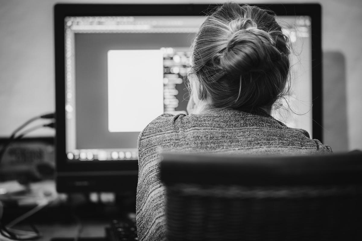 Femme assise devant un écran d'ordinateur, cheveux relevés en chignon