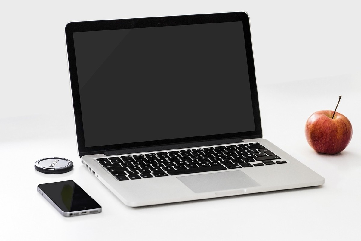 Laptop ouvert, smartphone, pomme et disque dur sur une table blanche