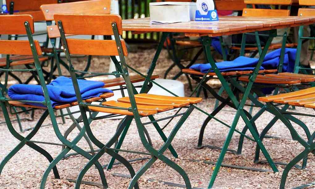 Mobilier de jardin composé de tables en bois, chaises pliantes vertes et coussins bleus, disposés sur du gravier