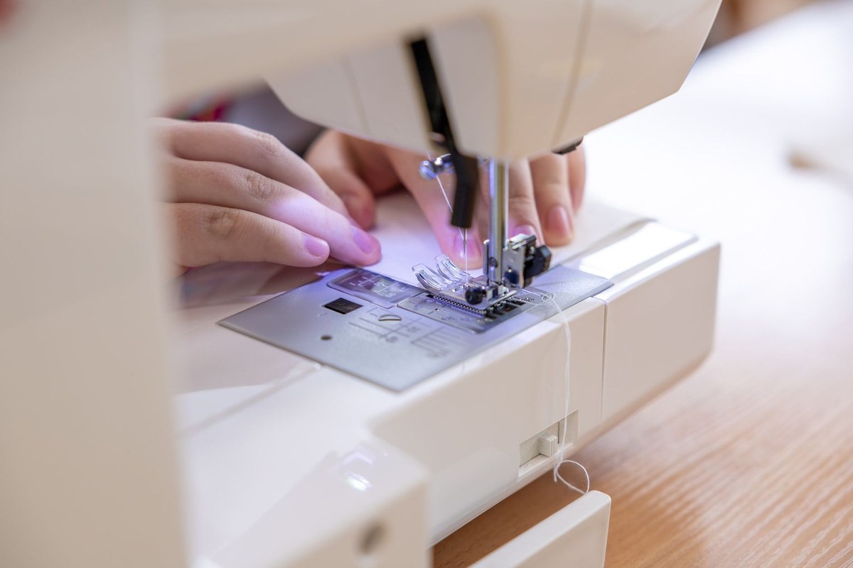 Mains utilisant une machine à coudre pour assembler un morceau de tissu